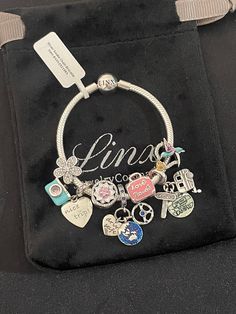 a bracelet with charms is sitting on a black bag and has the word love written on it