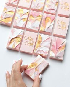 a woman's hand is touching some pink and gold marbled paper on a white surface