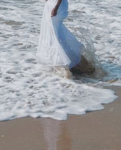 a woman in a white dress walking into the ocean