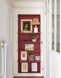 a red book shelf with pictures on it and a lamp next to the bookshelf