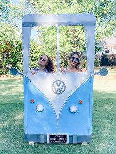 two girls are standing in front of a blue vw camper van shaped like a house