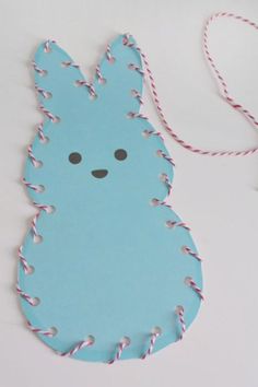 a paper bunny ornament hanging from a string on a white table with red and blue twine