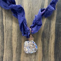 a necklace with a blue scarf around it and a stone pendant hanging from the front