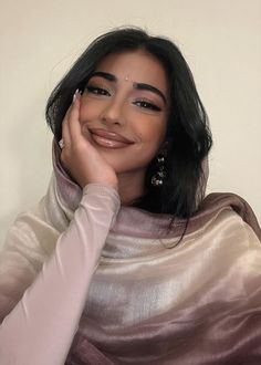 a woman with long black hair wearing a silver shawl and smiling at the camera