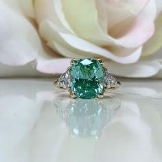 an emerald and diamond ring sitting on top of a table next to a white rose