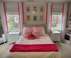 a bedroom with pink and white decor on the walls, windows, and bedding