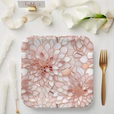 a place setting with pink flowers and gold cutlery on the side, along with napkins