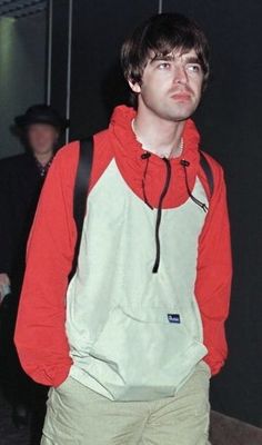 a young man in an orange and white hoodie looks up at the camera while wearing khaki pants