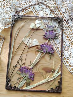 dried flowers are arranged in an old frame on a lace doily, with crocheted doily behind them