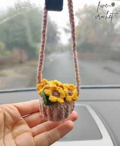 a hand holding a small crocheted sunflower on a car steering wheel handle