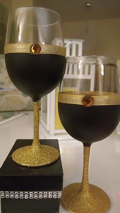 two wine glasses sitting on top of a black and gold box next to each other