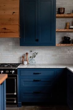 a kitchen with dark blue cabinets and white counter tops is pictured in this image, there are wooden shelves above the stove