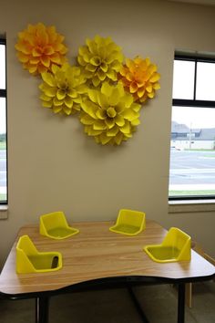 a wooden table topped with yellow chairs next to a large flower wall hanging on the wall