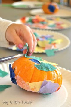 a child is painting a pumpkin on a paper plate