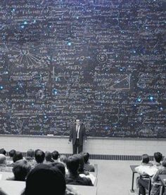 a man standing in front of a blackboard with writing on it and people sitting at desks