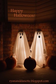 two halloween ghost standing next to each other in front of a brick wall with pumpkins