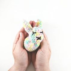 two hands holding a small stuffed animal in front of a white background with one hand over the other's face