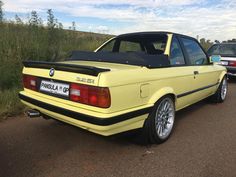 a yellow bmw is parked on the side of the road next to another car with its door open