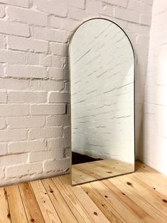 an arched mirror sitting on top of a wooden floor next to a white brick wall