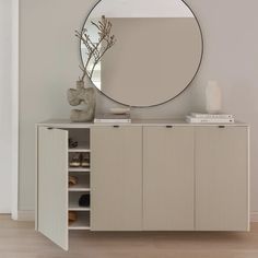 a large round mirror sitting on top of a wooden cabinet next to a white vase