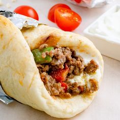 an open pita bread with meat and vegetables on the table next to some tomatoes