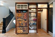 an open cabinet in the middle of a wooden floored room with stairs leading up to it