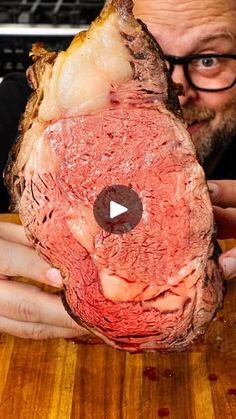 a man holding up a large piece of meat on top of a wooden cutting board