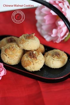 chinese walnut cookies on a black plate with pink flowers in the backgroung