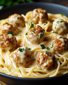 some meatballs and noodles are in a black bowl on a wooden table with parsley