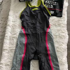 a black and grey one piece swimsuit laying on top of a white blanket next to a bottle of water