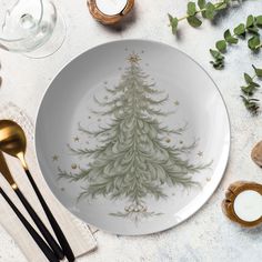 a white plate with a christmas tree painted on it next to utensils and candles