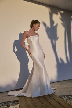 a woman in a white dress is standing on a wooden platform with her shadow cast on the wall behind her