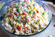 a glass bowl filled with macaroni salad on top of a wooden table