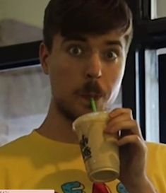 a young man drinking from a cup with a straw in his mouth and looking at the camera