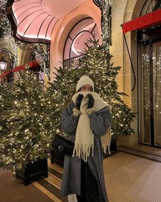 a woman standing in front of a christmas tree wearing a hat and scarf with her hands on her face