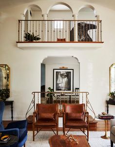 a living room filled with furniture next to a stair case above a fireplace covered in framed pictures