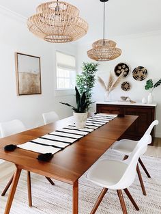 a dining room table with white chairs and hanging plants