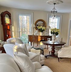 a living room filled with white furniture and lots of windows next to a table topped with flowers