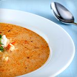 a white bowl filled with soup on top of a blue table cloth next to a spoon