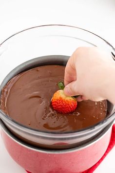 a person dipping a strawberry into chocolate in a bowl