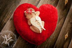 a red heart shaped box with a small angel on it's side, sitting on a wooden surface