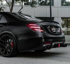 the rear end of a black mercedes cla parked in front of a tall building