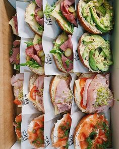 an open box filled with sandwiches covered in meat and veggies