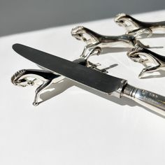 three silver figurines holding a knife on top of a white table with shadows