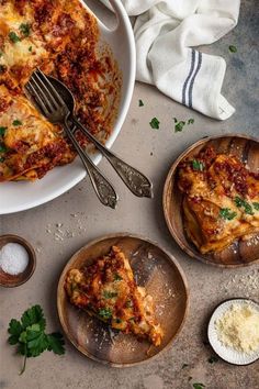 two plates with slices of lasagna on them next to a fork and spoon