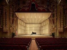 an empty auditorium with red seats and a piano on the stage in front of it