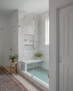 a white bathroom with a glass shower door and rug on the floor next to it