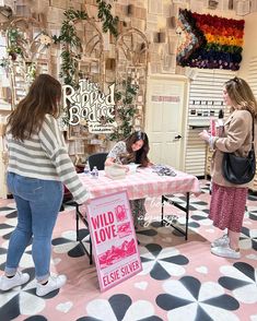 three women standing around a table with a sign on it