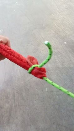 a hand holding a red and green rope with a knot on it's end