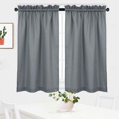 a dining room with a white table and gray curtains on the window sill, potted plant in front of it